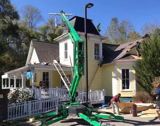 Green lift assisting roof repair on yellow house with white porch