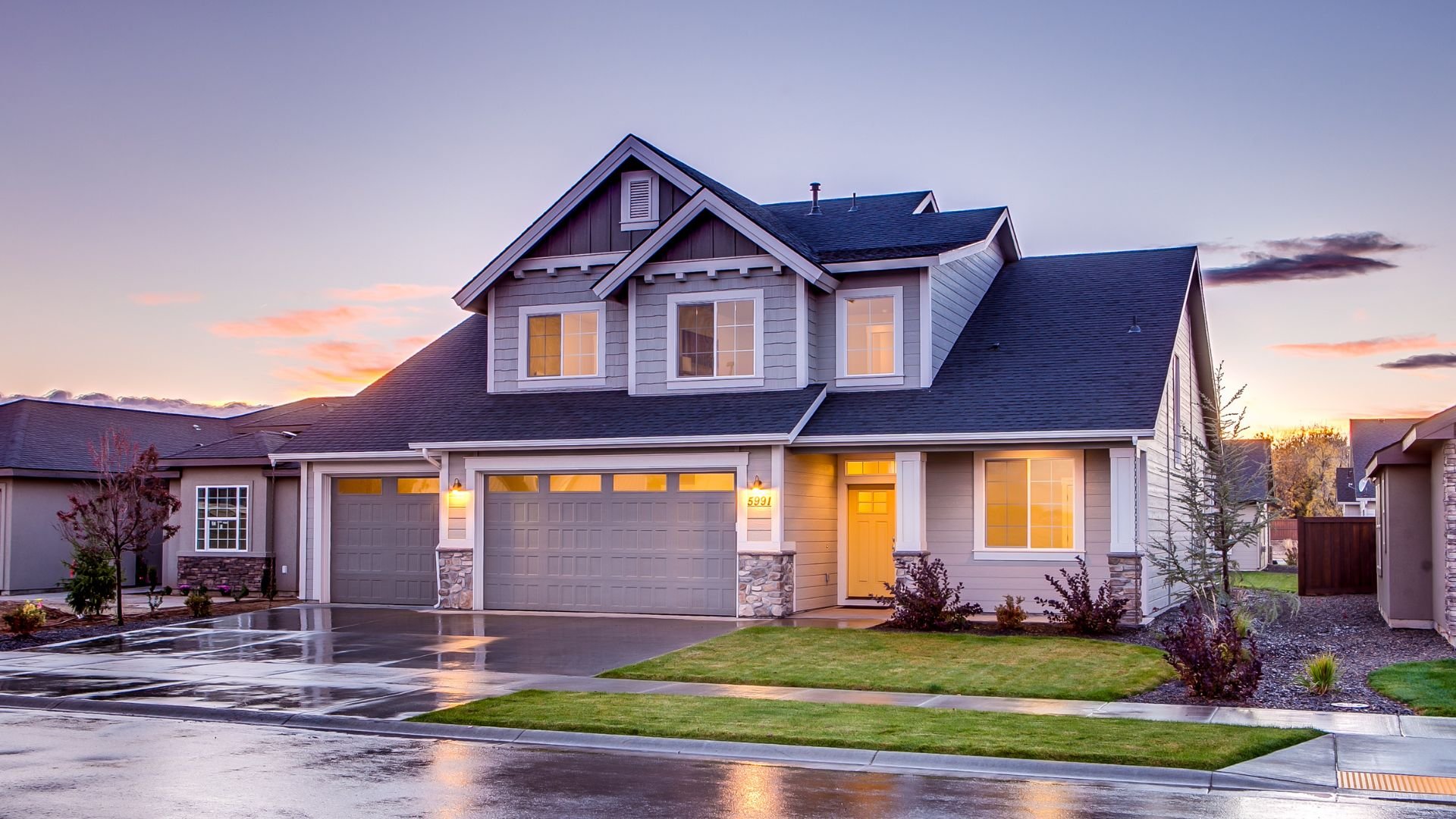 Modern two-story house with glowing windows at sunset, wet driveway