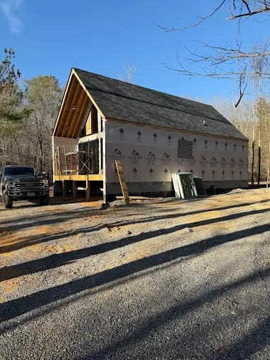 Wooden barn under construction with truck parked on gravel road