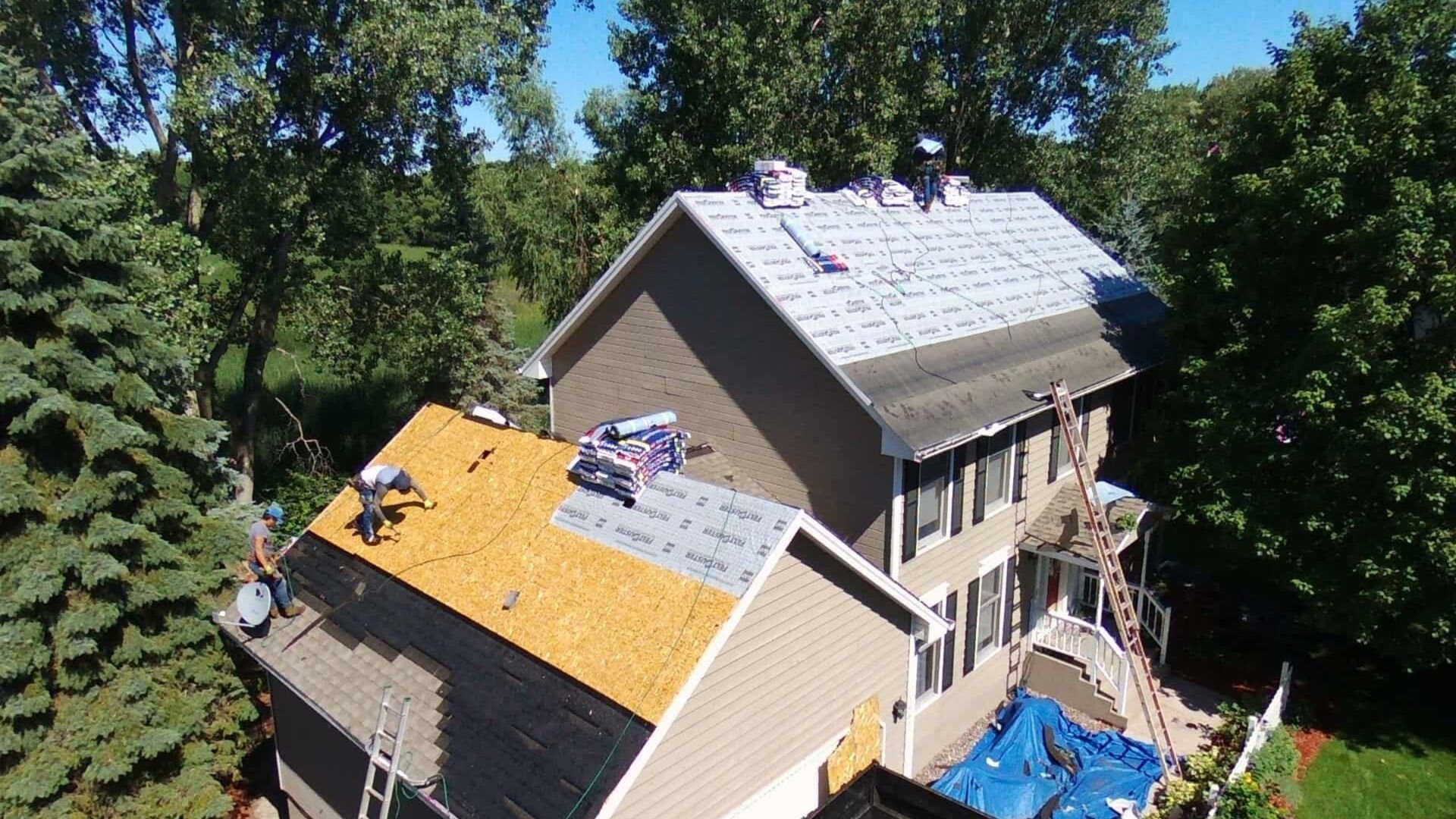 Aerial view of roofers installing new shingles on a two-story house