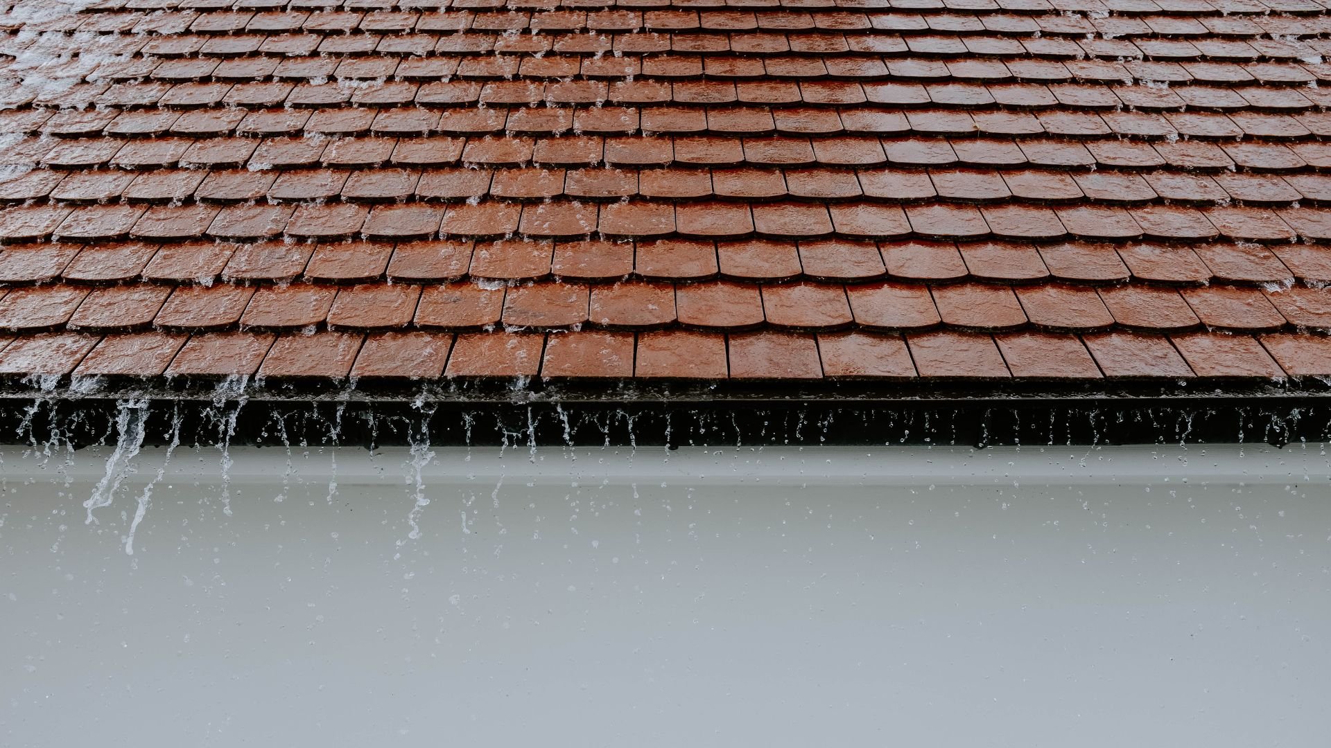 Rusty red roof tiles with water dripping down during rainfall