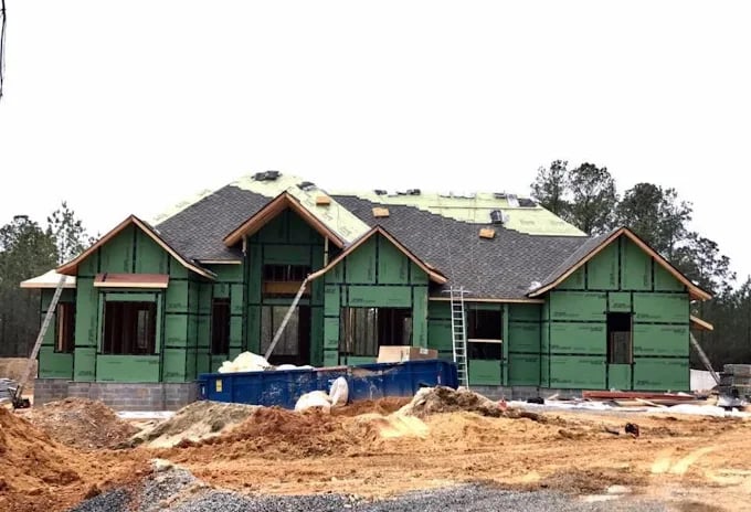 Large green house under construction with blue dumpster and wooden framing