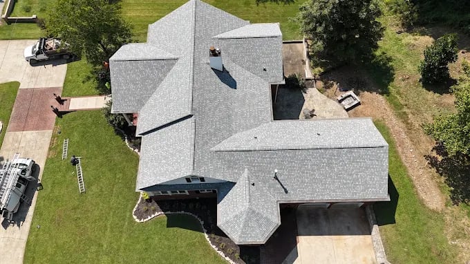 Aerial view of large gray-roofed house with surrounding green lawn and vehicles