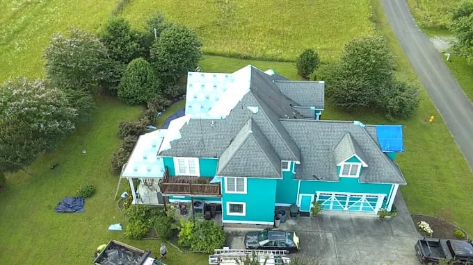 Aerial view of teal two-story house with gray roof on green landscape