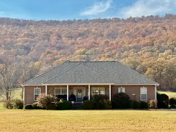 Brick ranch house with front porch, autumn forest and hills in background