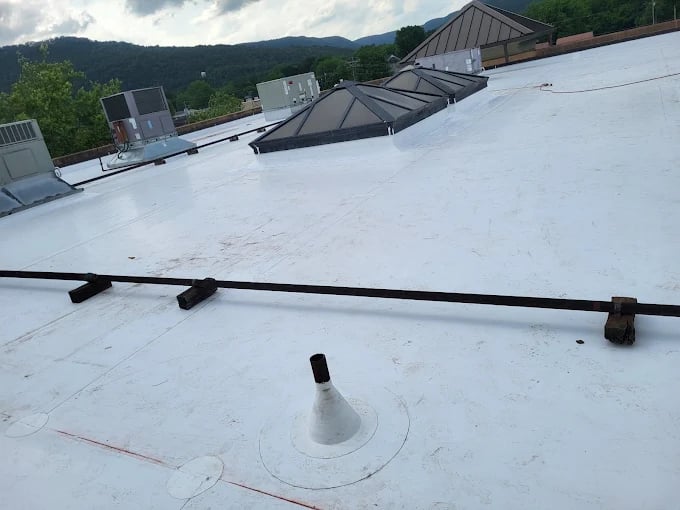 White flat roof with mechanical equipment, ventilation units, and mountain backdrop